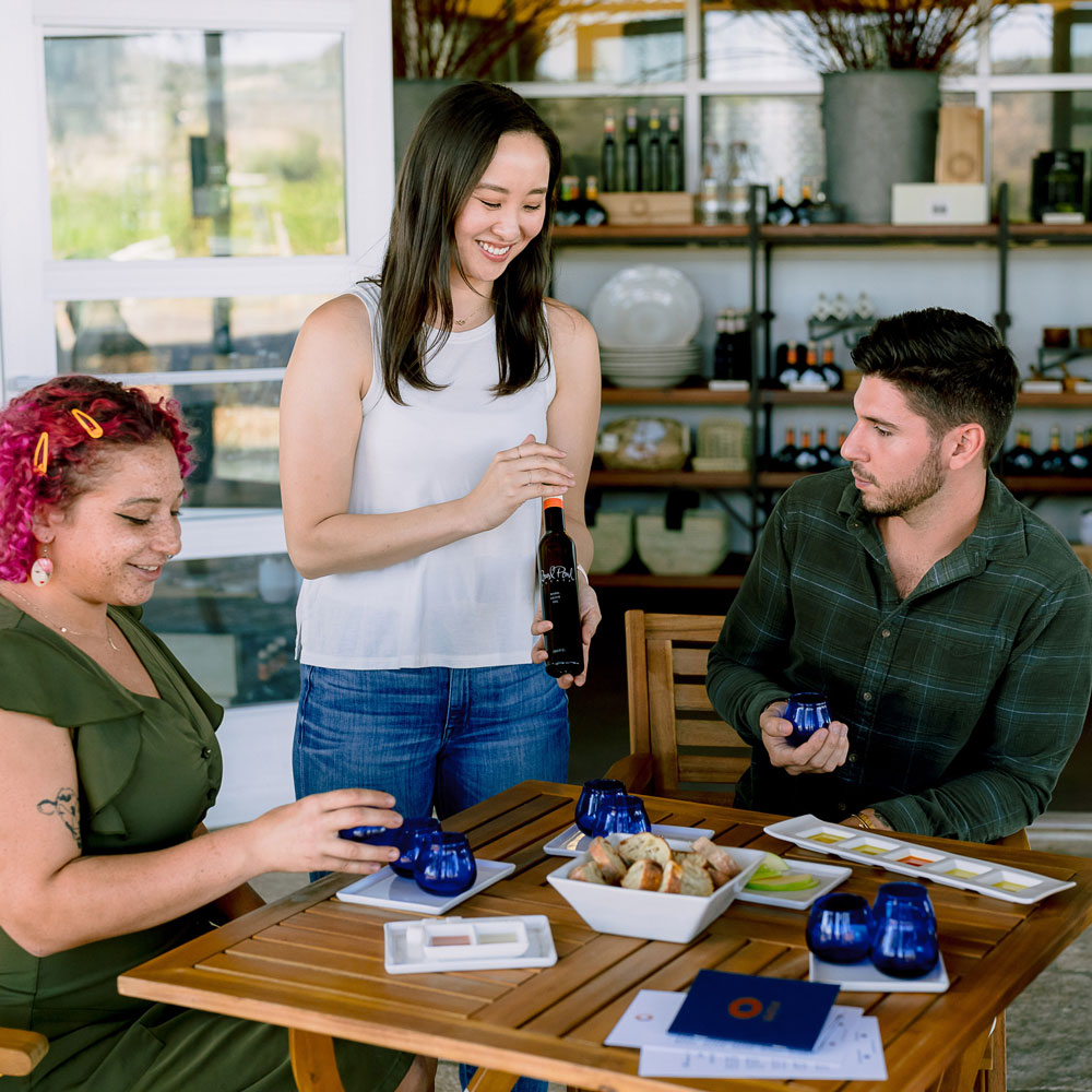 A server presents a bottle of Round Pond Estate Infused Olive Oil to two guests seated at an olive oil tasting.